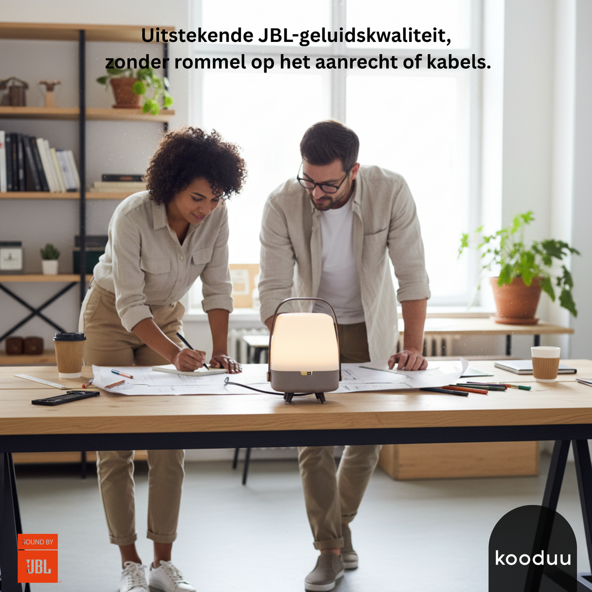 Two people working at a desk with a Kooduu lamp, JBL logo visible.
