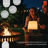 Two people roasting marshmallows over a campfire with a kooduu lantern and JBL branding.
