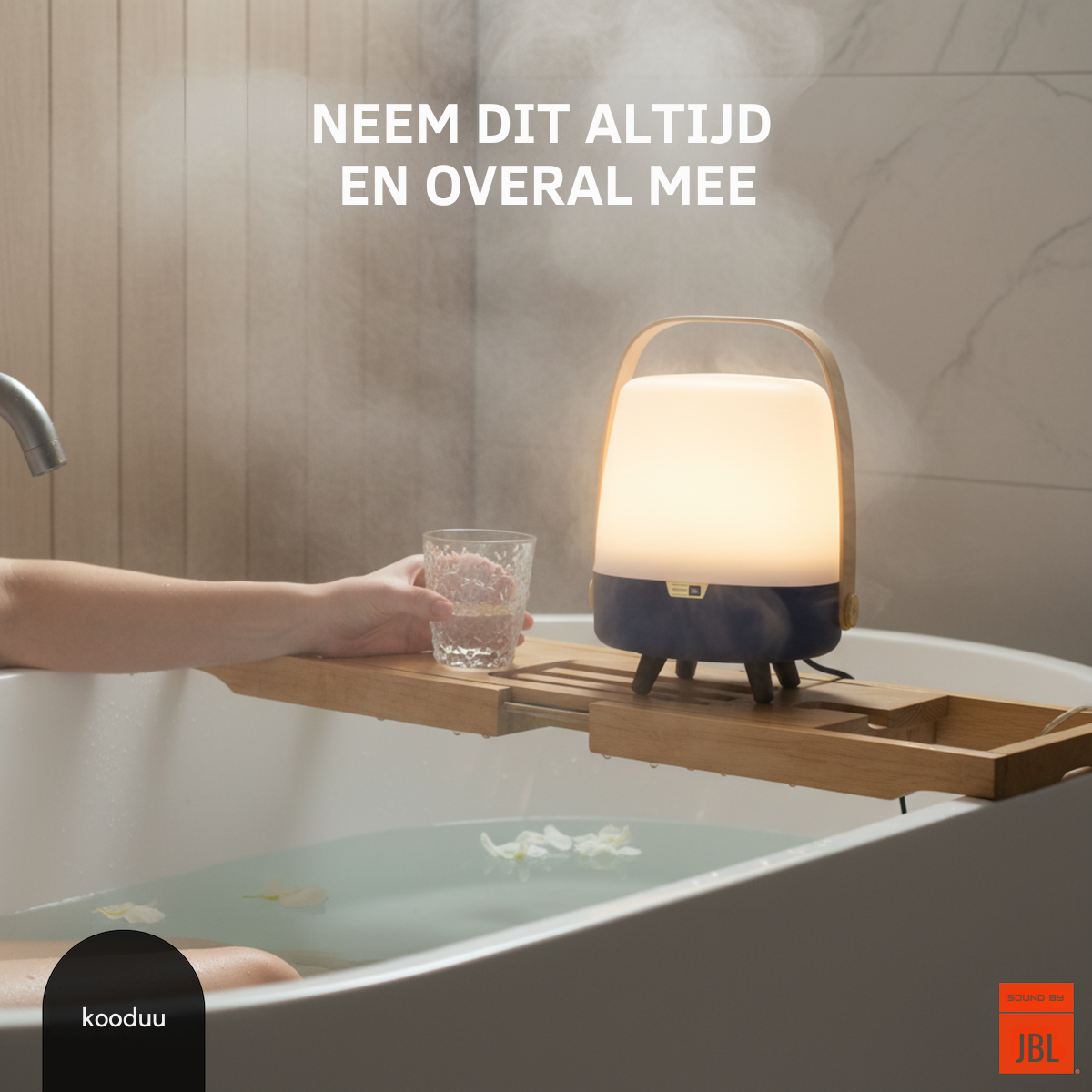 Person holding a glass of water next to a lamp on a bathtub tray with 'kooduu' and 'JBL' branding.