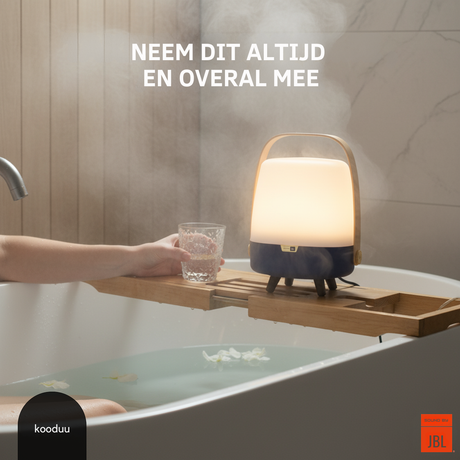 Person holding a glass of water next to a lamp on a bathtub tray with 'kooduu' and 'JBL' branding.