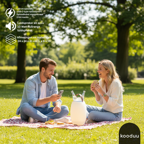 Two people sitting on a blanket in a park with a KOODU SYNERGY 35, surrounded by trees and greenery.